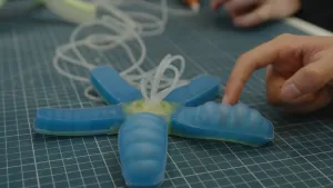 Een foto van een soort zeester van siliconen rubber. In de armen van de zeester zitten luchtkamers. In twee armen wordt lucht geblazen, die armen gaan krommer staan. Een vinger wijst ernaar.