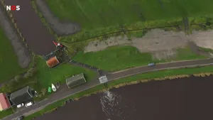 Een drone-foto van een gebouw naast weilanden. Een grote sloot loopt langs de weilanden. Over de weg lopen pijpen die water lozen in een naastgelegen meer.