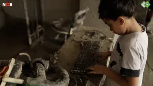 Een foto van een kind dat typt op een toetsenbord dat vol modder zit door de vloedgolf in Nepal.