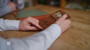 Een foto van een oude bruine leren portemonnee. Er zit een zwart-witfoto in. De portemonnee wordt aan tafel vastgehouden door twee mannenhanden.