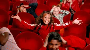 Foto van kinderen op rode pluche stoelen.
