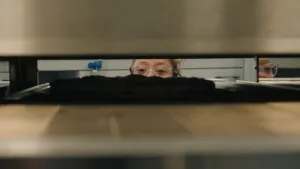 Een foto van een meisje met een bril dat in een grote oven kijkt of de pizza al klaar is.