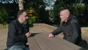 Een foto van twee mannen aan een picknickbank. Beide worden ze grijs. De ene is van Turkse afkomst en heeft een baard, de andere is van Nederlandse afkomst en heeft een sikje en zijn haar aan de zijkanten opgeschoren.