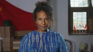 Presentatrice Astrid staat midden in het beeld en kijkt in de camera. Achter haar een rode vlag en een raam met daarin vlaggetjes.