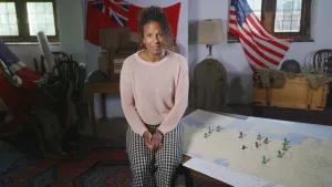 Presentatrice Astrid zit op een tafel en kijkt in de camera. Op tafel ligt een kaart.