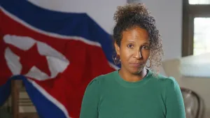Presentatrice Astrid kijkt in de camera. Achter haar hangt een vlag van Korea.