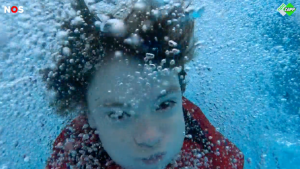 Een close up foto van een kind onder water, er zitten allemaal belletjes rond het gezicht.