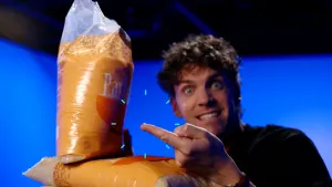 Foto van presentator Benjamin met een rijstkorrel op zijn vinger naast grote zakken met rijst in Jeugdjournaal studio.
