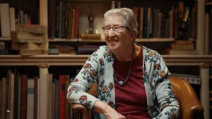 Foto van grijze dame van 92 met bril voor een oude boekenkast.
