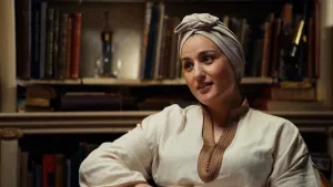 Foto van actrice Nora Akachar voor een houten boekenkast.