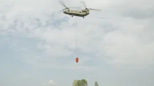 Foto van een helikopter met een grote zak water die eronder hangt.